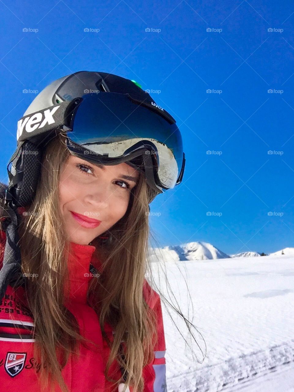 Portrait of woman with Uvex ski glasses and helmet with snowy mountains in the background