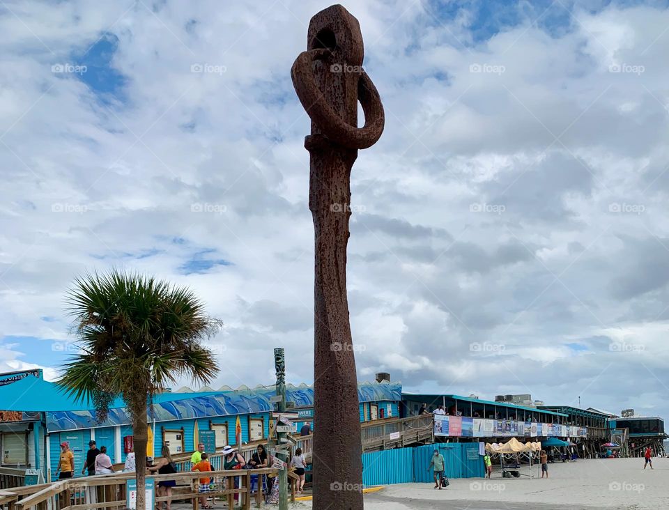 Visiting the visitor touristic pier in Cocoa Beach as a family for the first time in central eastern Florida looking at the immense old historic tall anchor with many shops, restaurants, business and boutiques at the Atlantic Ocean beach with crowd.