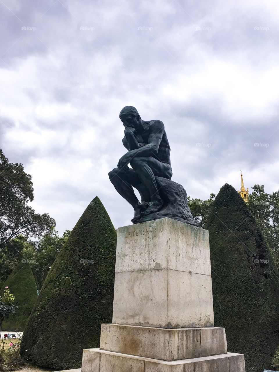 A picture of The Thinker at the Rodin museum in Paris. He is against a cloudy sky.