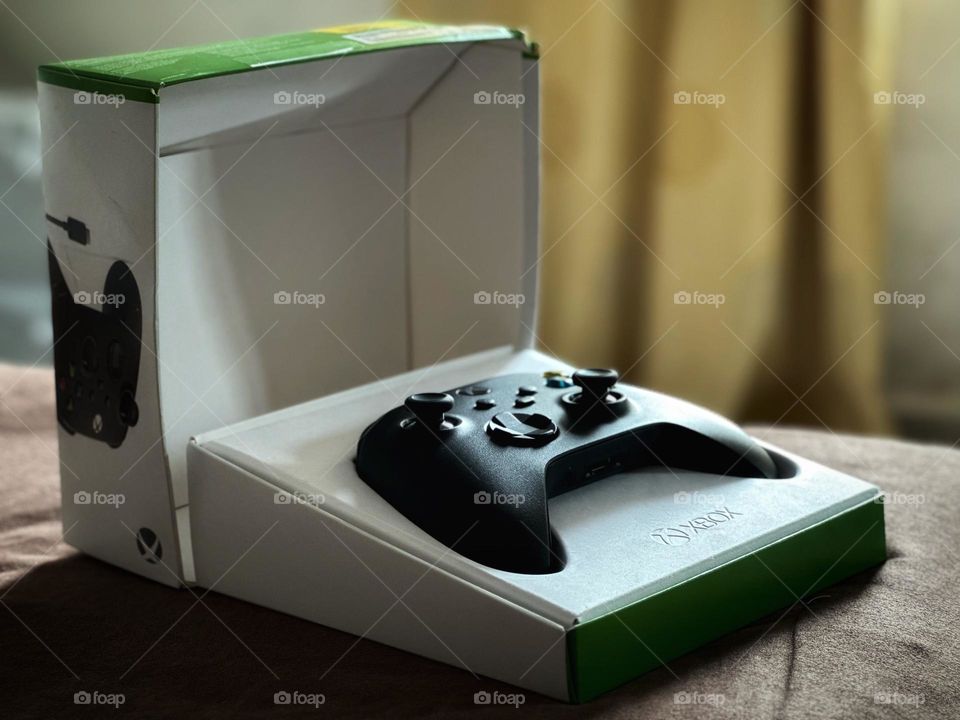 Black Xbox controller inside of its box just opened while the natural light enters through the window.