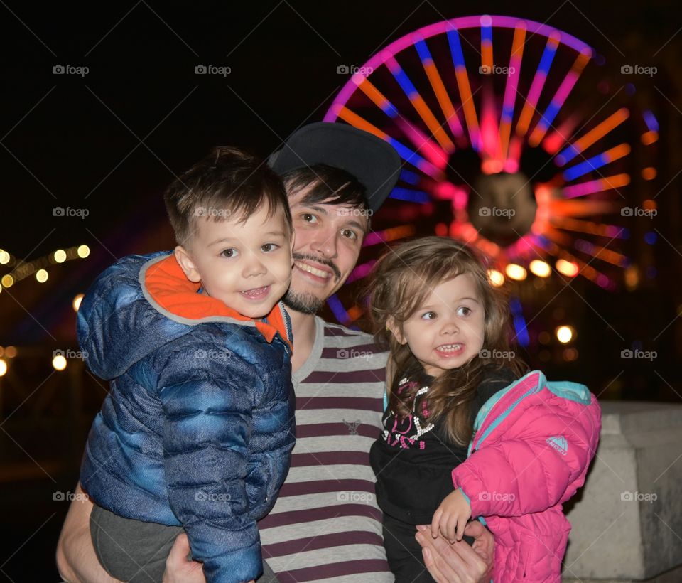 Man holding children against illuminated wheel