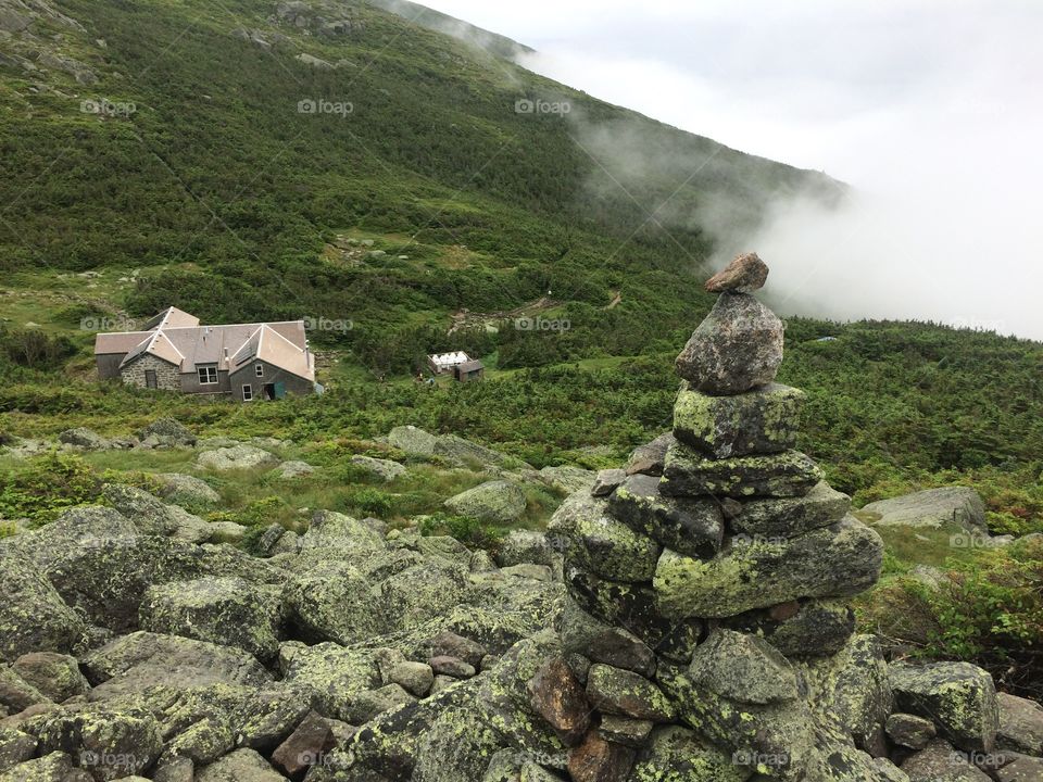 A cairn marks the trail up Mount Madison with the hikers hut below in the white mountains of New Hampshire