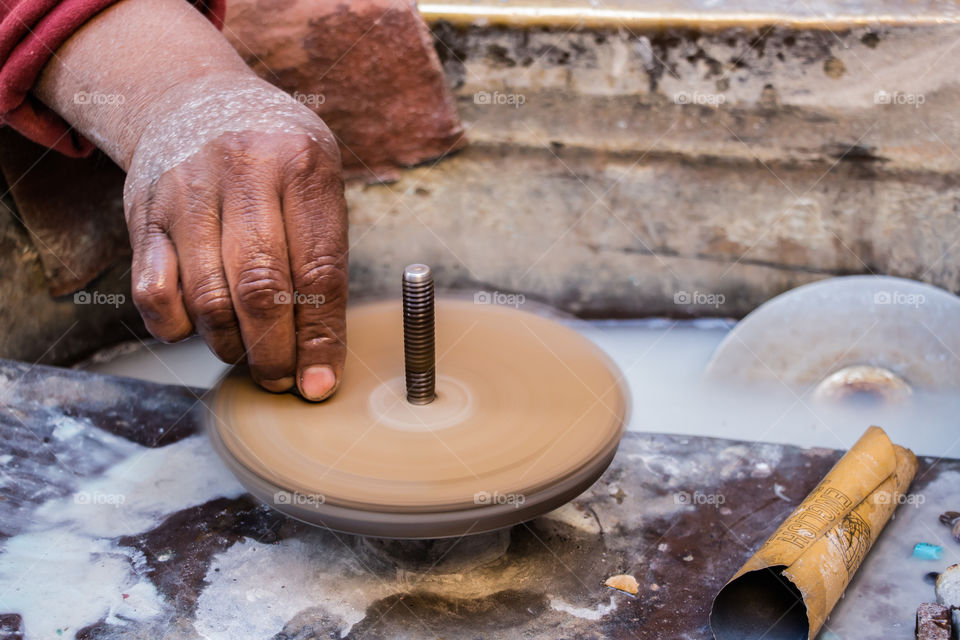 This man's job is to use this machine to turn big stones into lovely little soft and clear pieces of gems, to be used later as accessories or part of decoration. You will see different angles of the same hand and job.