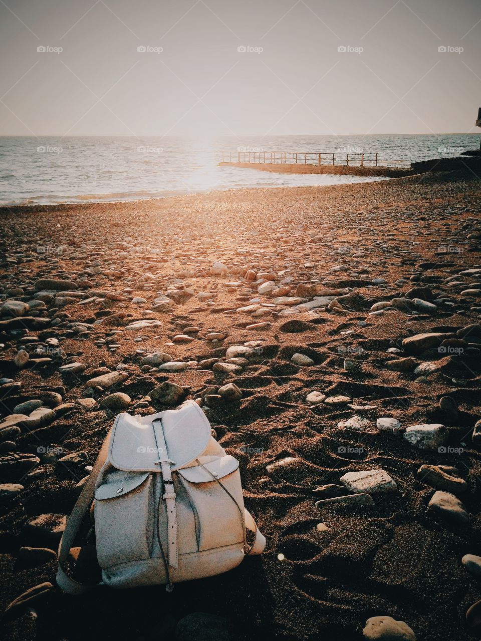 Sunset beach with stones and white rucksack.