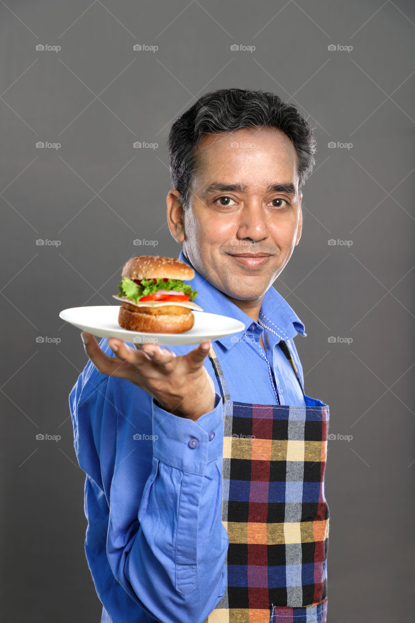 Indian man chef with a burger in a hand