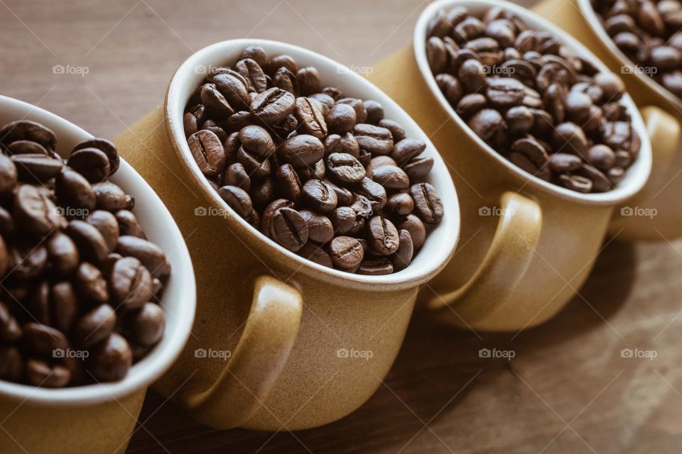 A diagonal row of 4 coffee cups, filled with coffee beans against a wood background.