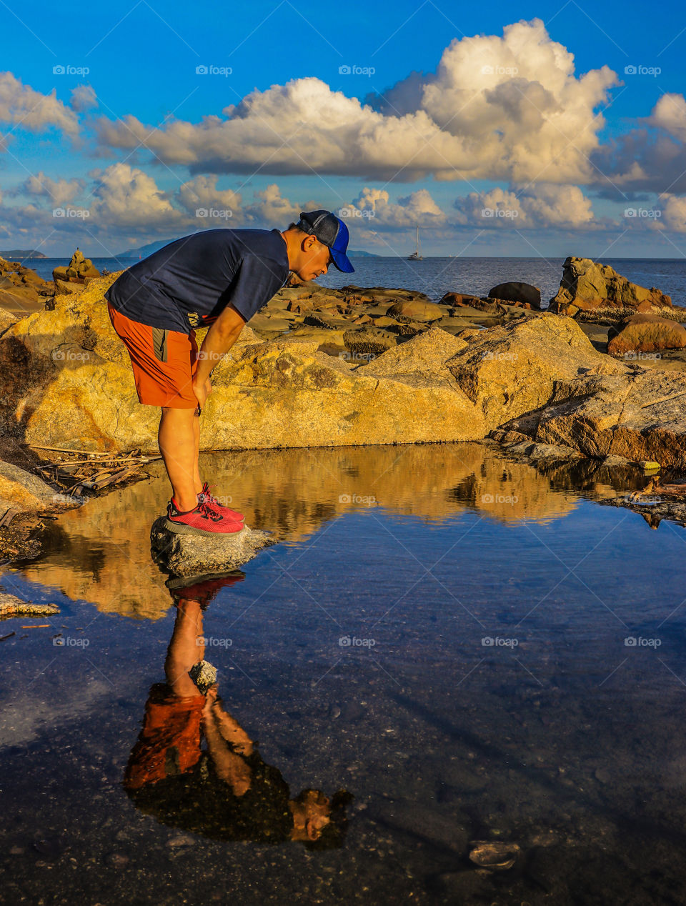 A man observing some marine species on a pond at a nearby Beach during the day time. The reflections from the water, the blue skies, ample clouds and the rock formations caught my interest.