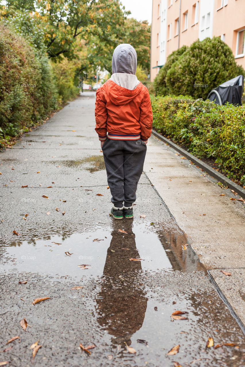 Rear view of boy reflecting in puddle