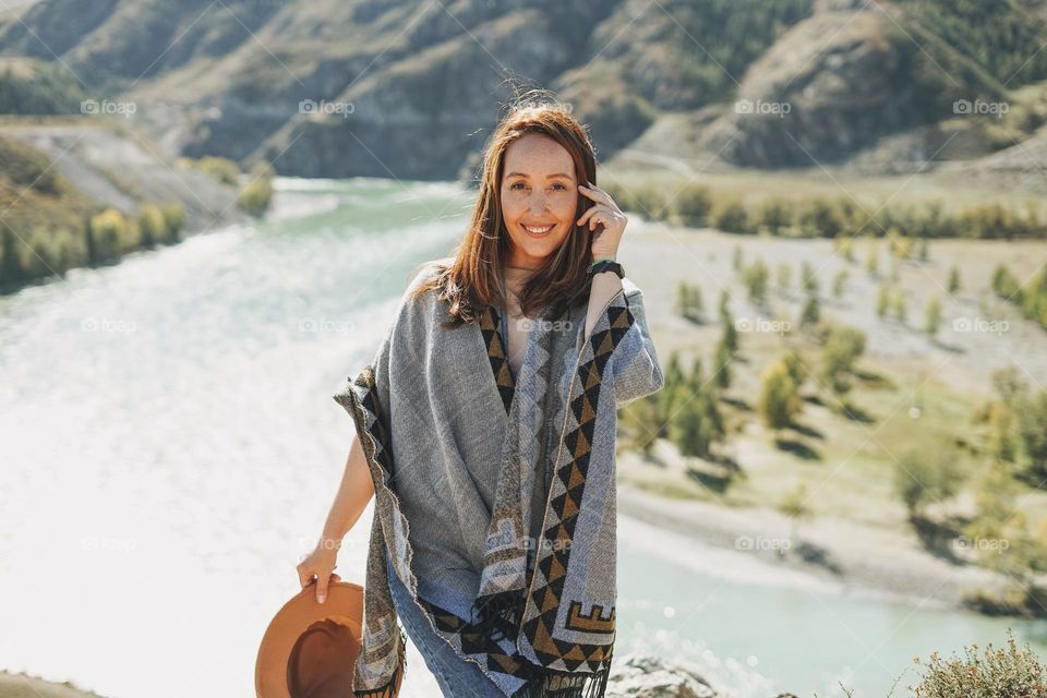 Carefree brunette young woman traveler in poncho on background of mountain river