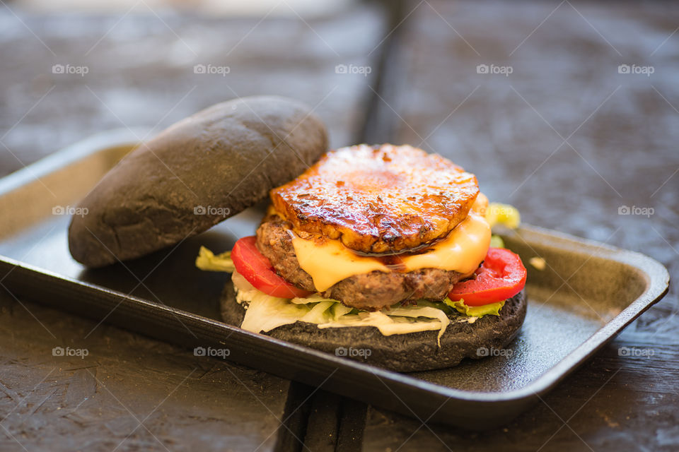 Black burger with grilled pineapple and spicy sauce on street food festival