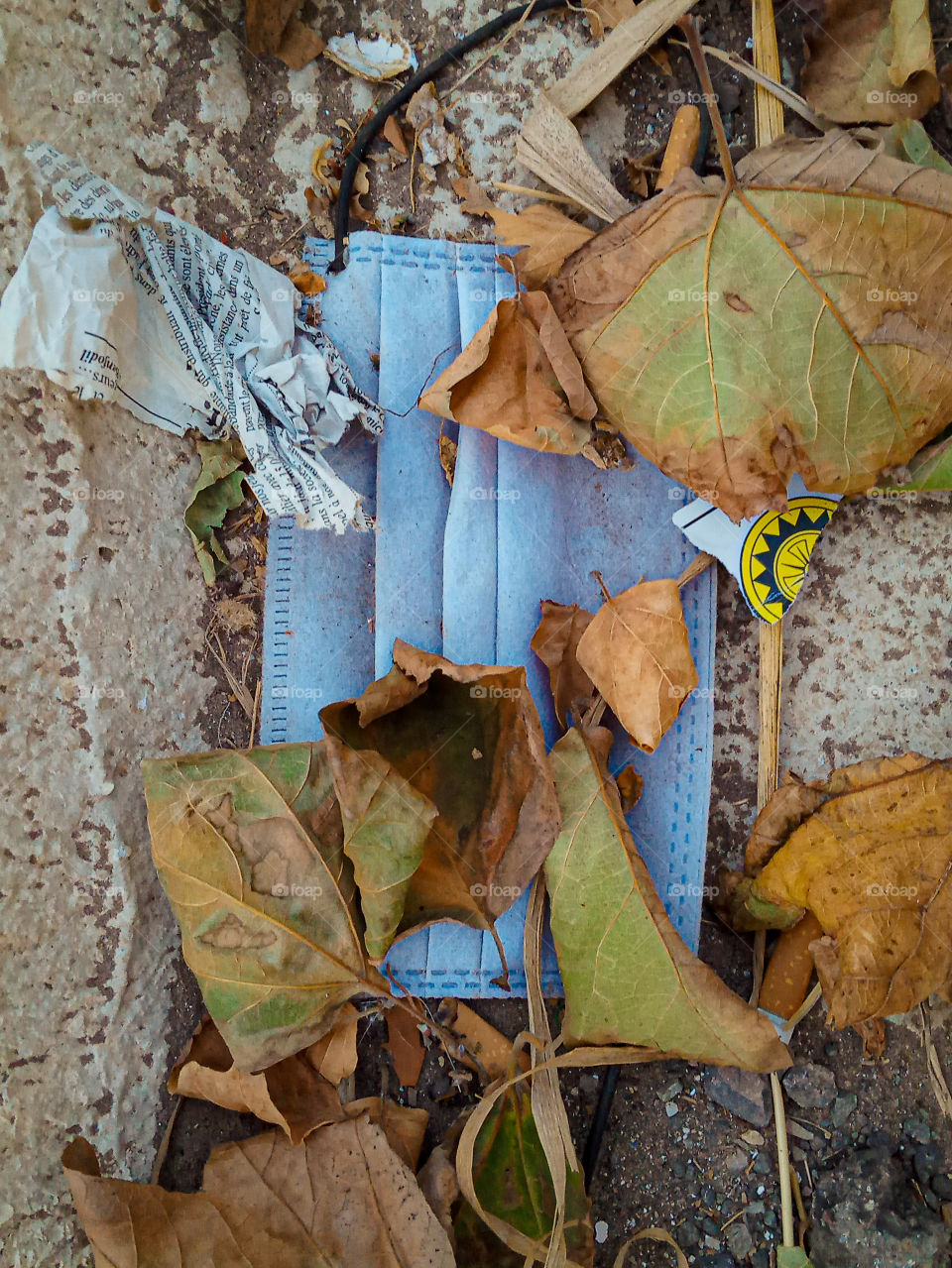 a surgical mask thrown on the floor with drie leaves and sheets of card and journald