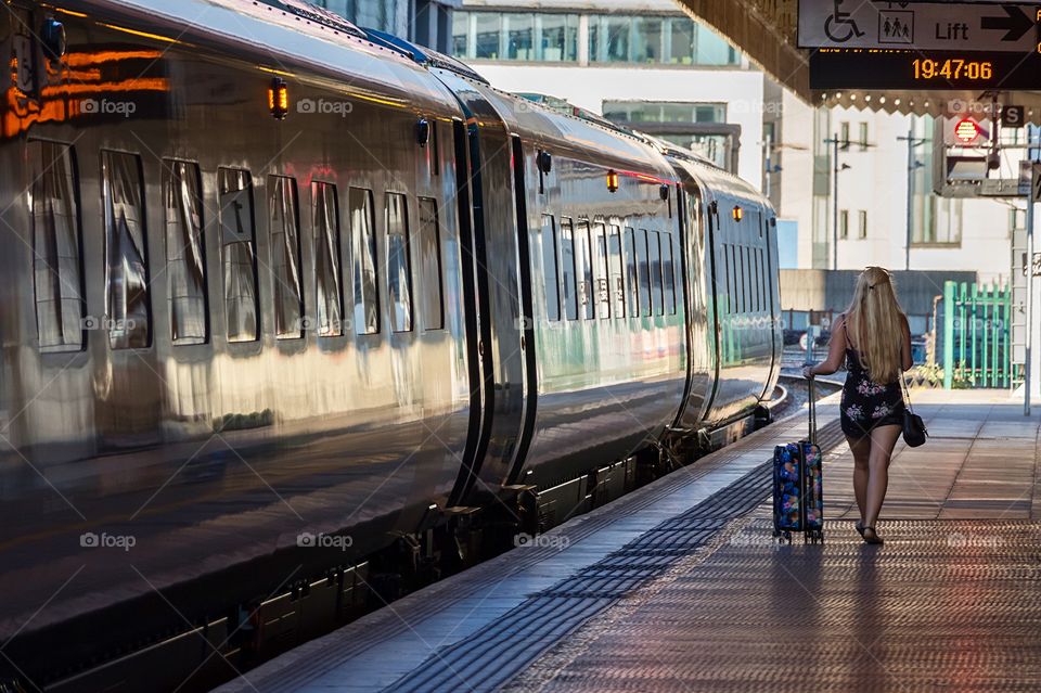 Back side view of girl with a suitcase at train station in Cardiff, Wales, UK
