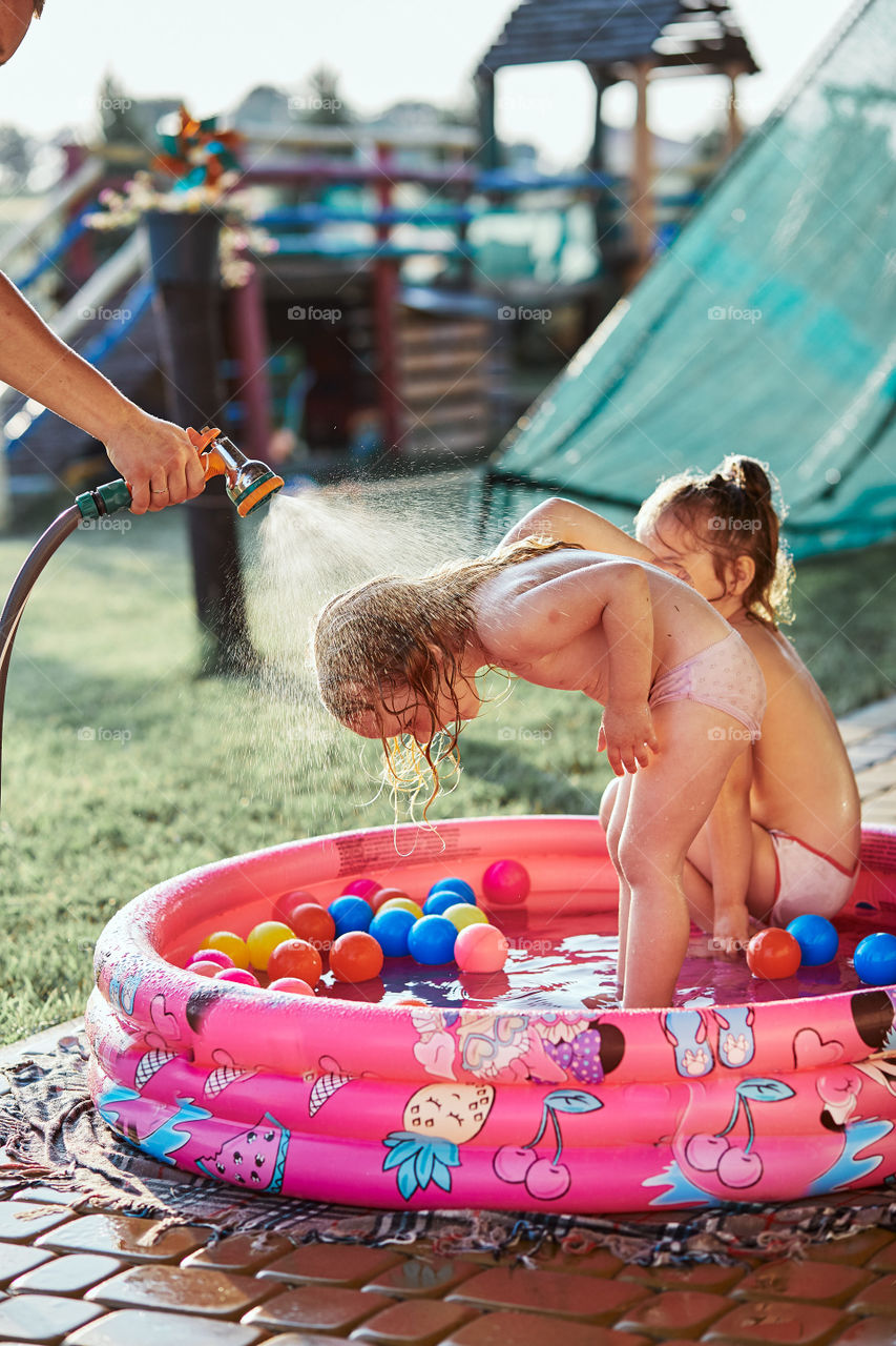 Little cute adorable girls enjoying a cool water sprayed by their father during hot summer day in backyard. Candid people, real moments, authentic situations