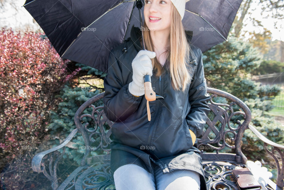 Young woman sitting on a bench outdoors with an umbrella in the winter