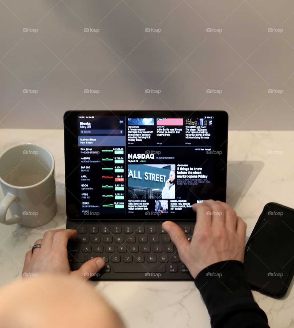 Man searching stock on Apple’s Stock App on a Gen 7 iPad with coffee cup and Iphone 11 Pro Max