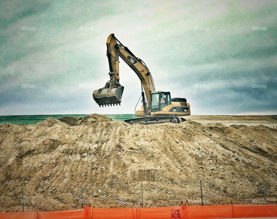 An Earth Excavator moves dirt at a roadside grading project.