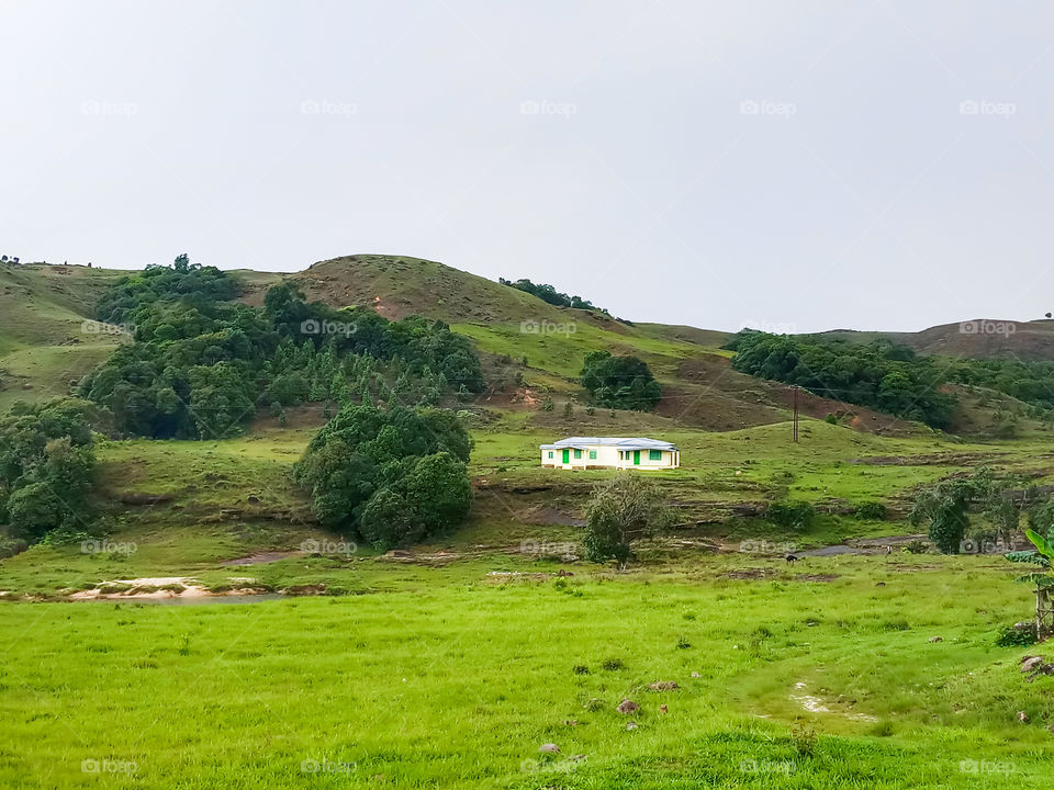 one small isolated cabin or house in the middle of the valley surrounded by green fields