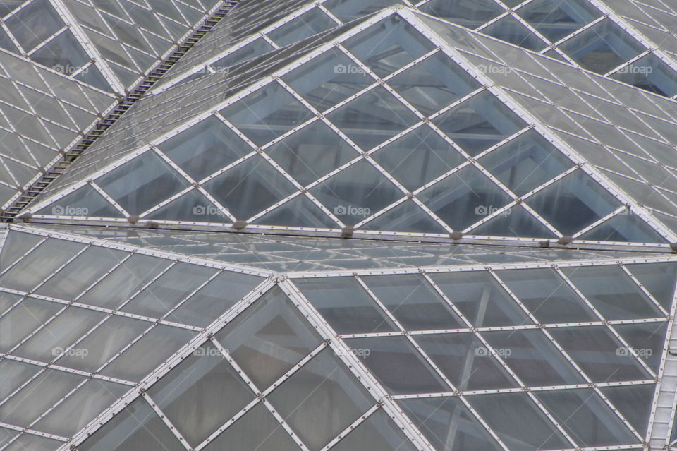 A closeup of the glass pyramid-shaped roof of a building. The light on the pyramids of glass creates different colours of brown and grey and the cross beams create  depth and an interesting pattern. 