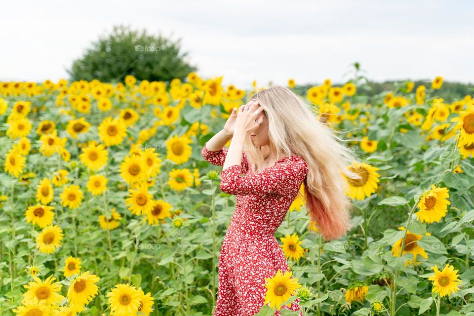 a girl with long blond hair stands in a field of sunflowers