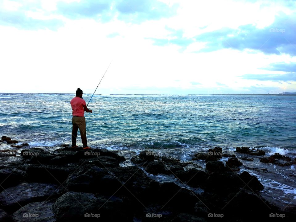 Deep blue Sea, man is fishing although the weather is windy, cloudy and the sea is rough.