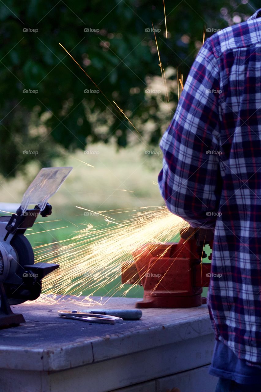 Side view of sparks from a bench grinder being used by a man on a steel part
