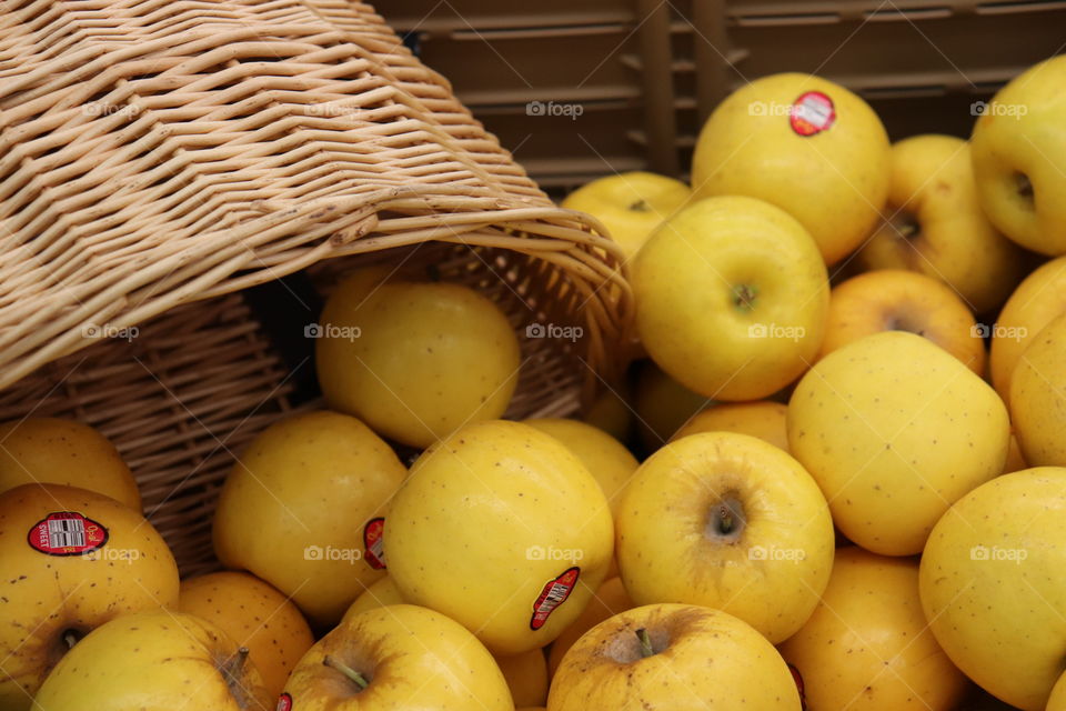 Bright yellow apples with stickers tumbling out of a basket into a bin close up in a market