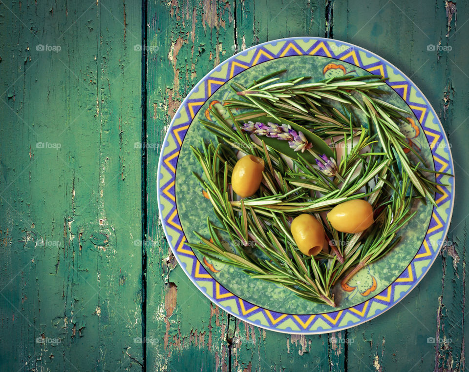 The concept of simple, healthy natural food and seasonal vegetables . Olives and rosemary sprigs on an ornamental plate on an old wooden table top. Food photos, horizontal orientation, top view