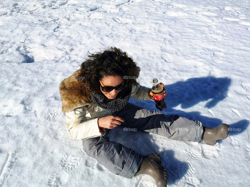 woman sitting on the snow drinks Coke and pours it on herself