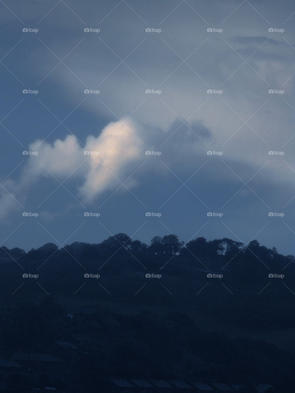 A lighter cloud in front of the dark ones over a hill