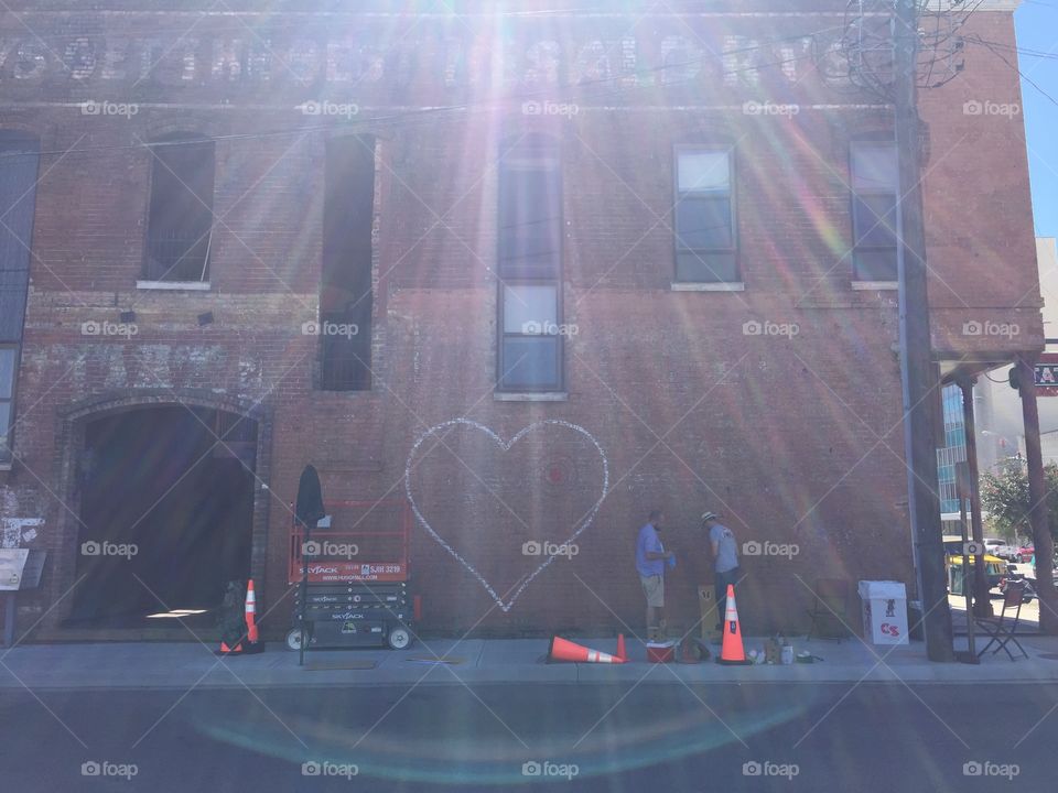 Two street artists are bathed in sun rays as they paint a wall mural. 