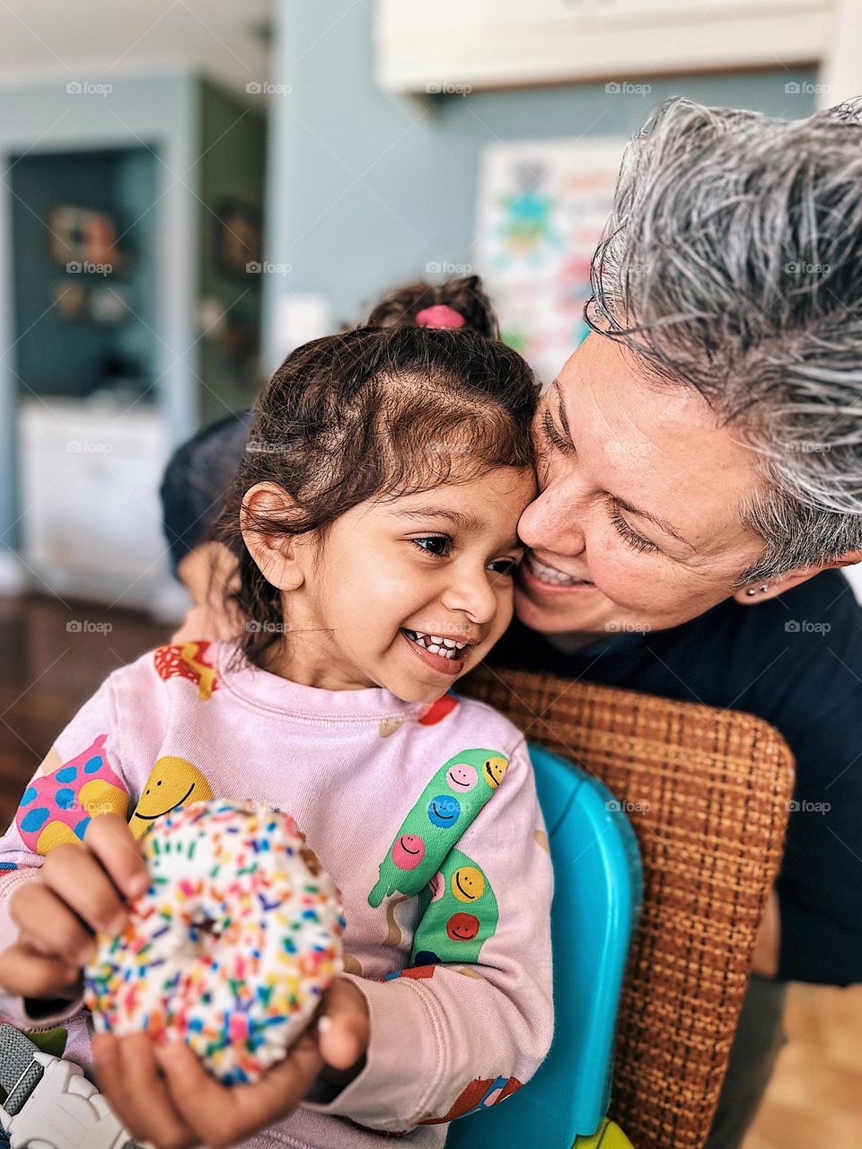 Portrait of mother and daughter enjoying a donut, toddler and mother laughing, mother surprises toddler while eating a donut, toddler eating a donut, mother and toddler enjoy breakfast, eating donuts with kids, mobile photography, smartphone photo 