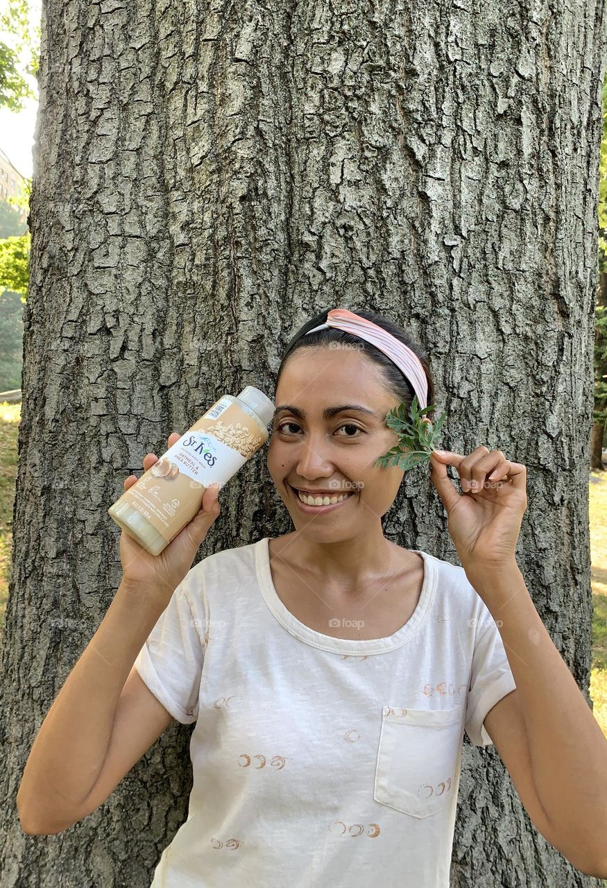 Energetic person holding St. Ives oatmeal shea butter soothing body wash against a big tree. 