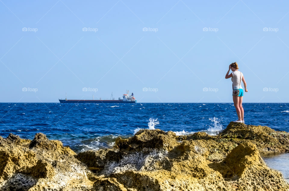 Woman on a rocky shore with an oil tanker anchored on the horizon