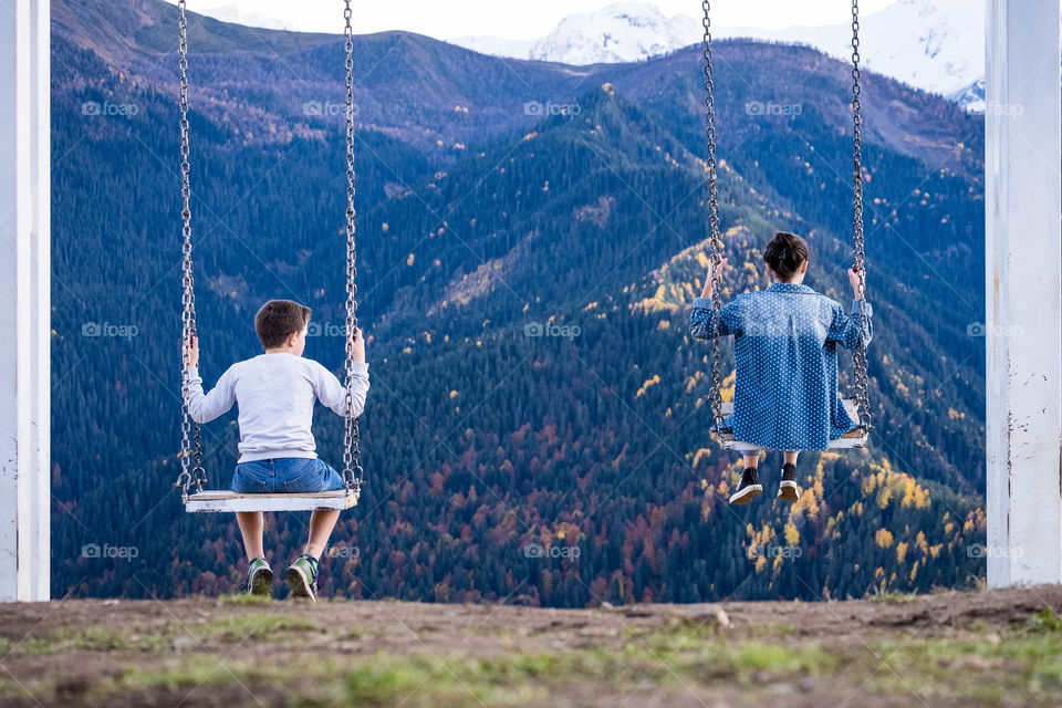 Boy and his older sister play swing together in beauty autumn season