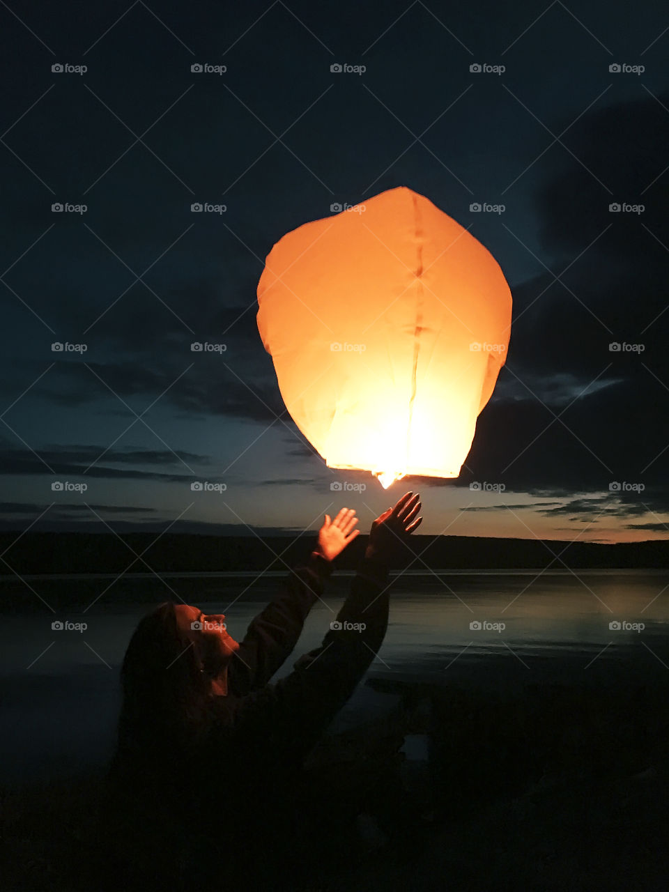 Young woman running Chinese lantern into the evening sky at the lake 