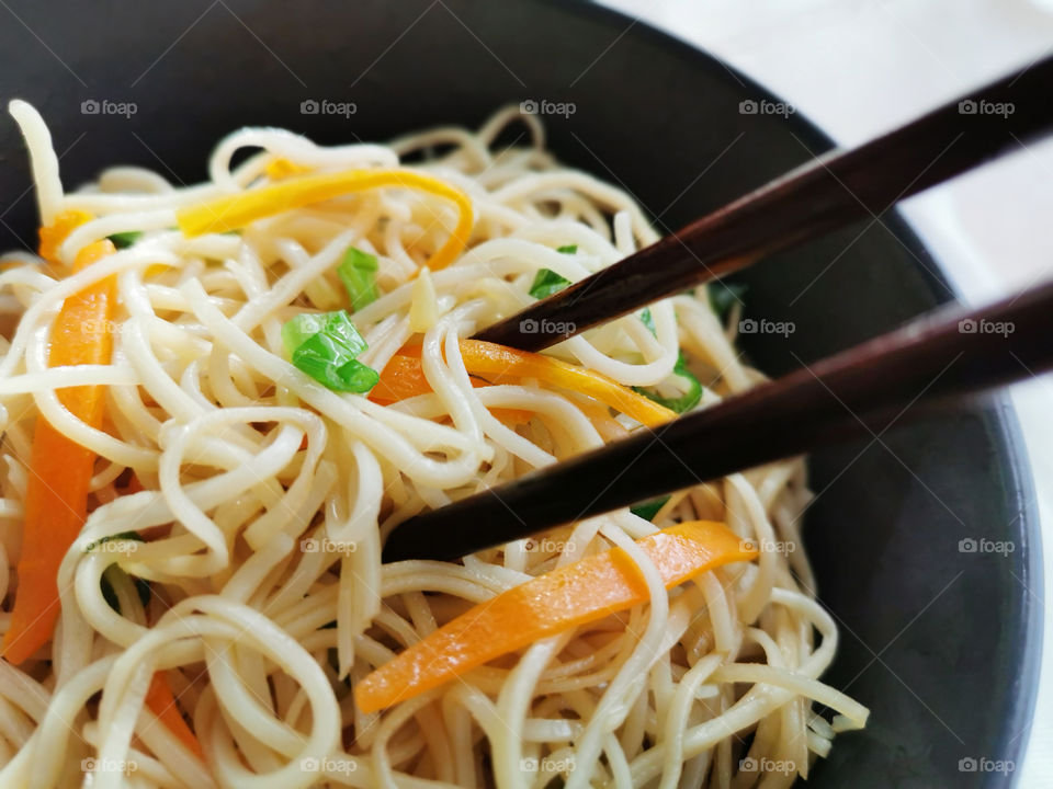 Chow mein with vegetables in a black bowl with chopsticks.