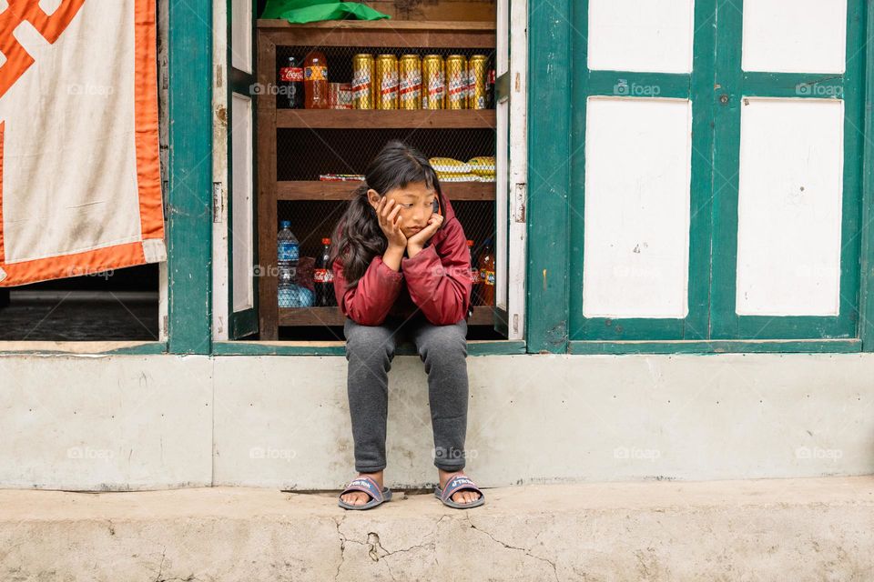 Young beautiful nepali girl being sad, while sitting in front of a small shop.
