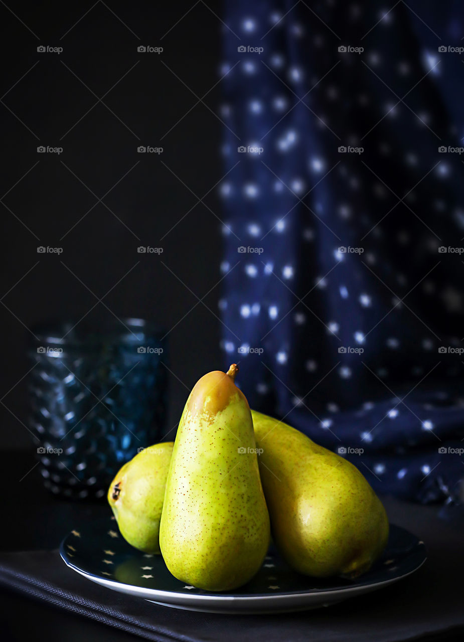Dark still life with pears. Green ripe sweet pears on a plate on a dark blue background. The concept of natural seasonal fruits on your table. Food photo, vertical orientation, copy space