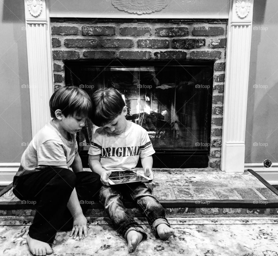 Brothers sitting near fire place in house with tablet
