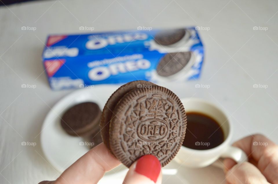 A woman’s fingers holding an Oreo cookie and a cup of coffee