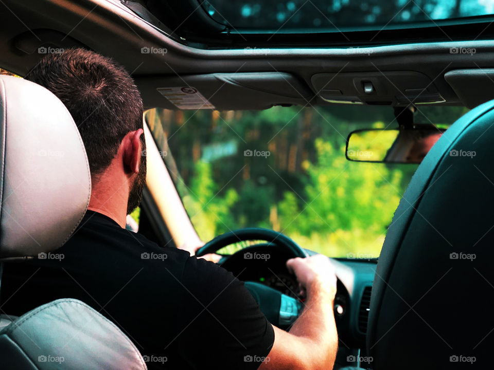 Young man driving a car through the forest road 