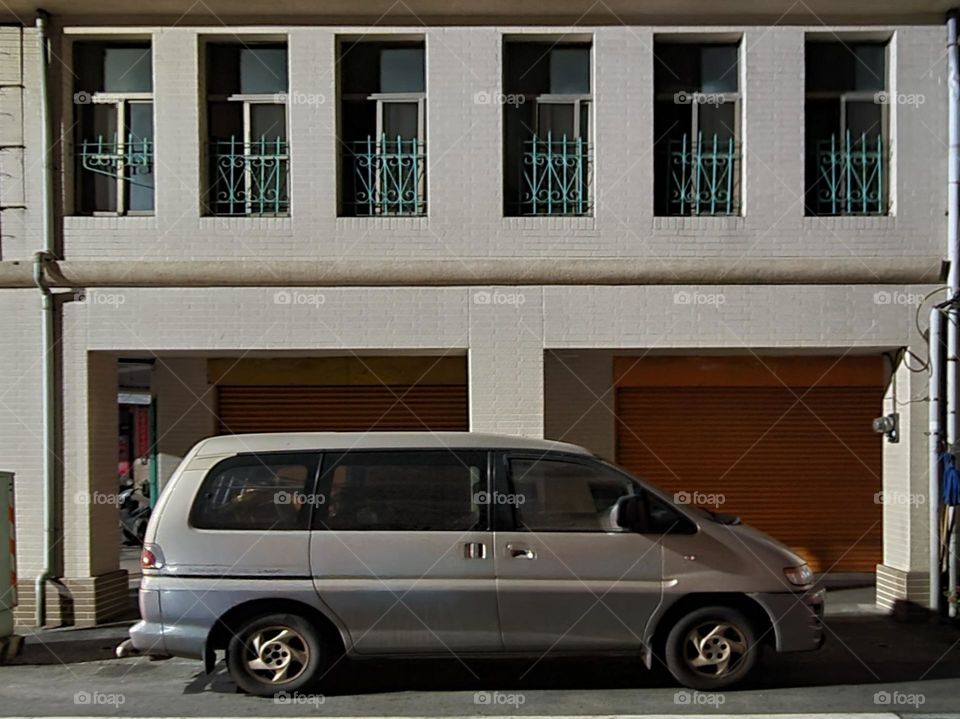 The car is parked in front of a white building with orange iron rolling doors