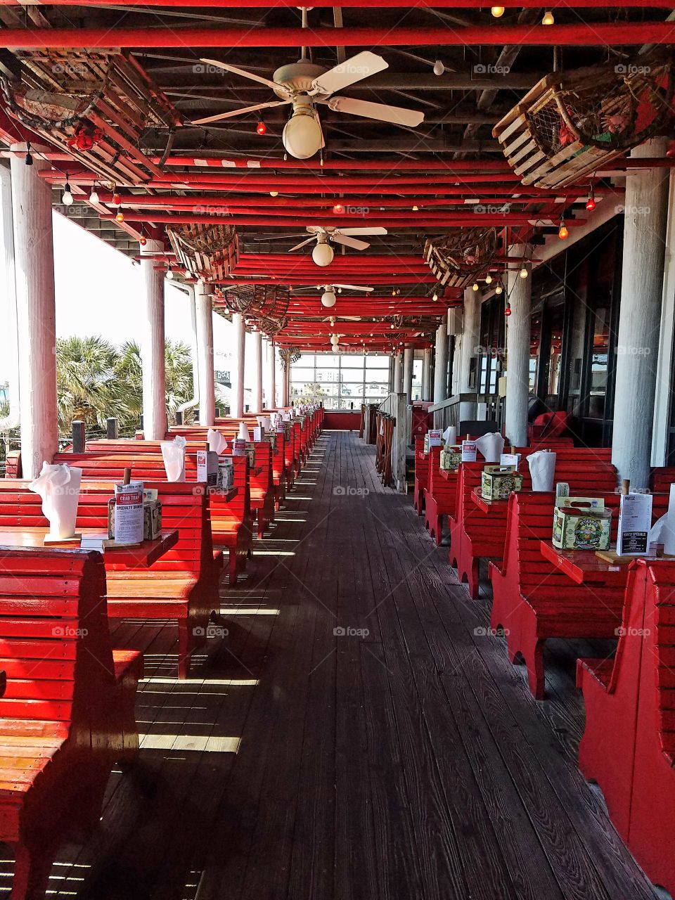 Red tables and bench seats at beach front restaurant on Pensacola Beach Florida.  Natural wood floors , white pillars and ceiling fans. architecture in perspective.