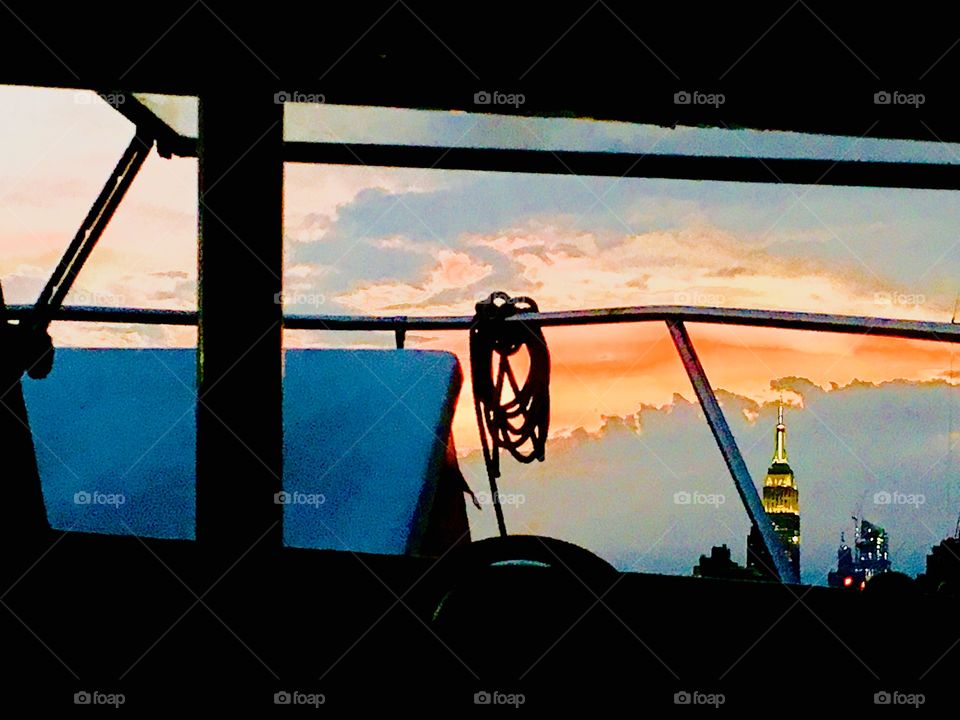 The illuminated Empire State Building as seen from aboard the “Salvation” our sailboat in Newtown Creek, Long Island City, Queens, NY. The white hutch cover appears blue in the twilight of dusk and nightfall. Photo from 2018. Hypnotic Productions