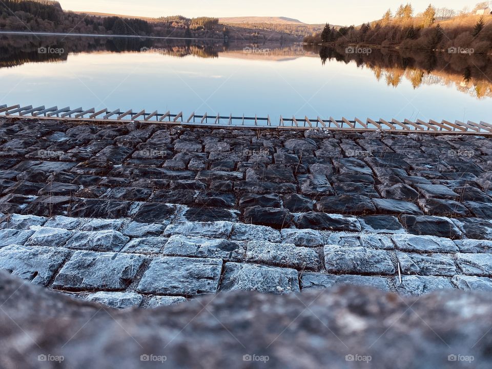 Perfectly still water reflecting the surroundings, with frozen stone. 