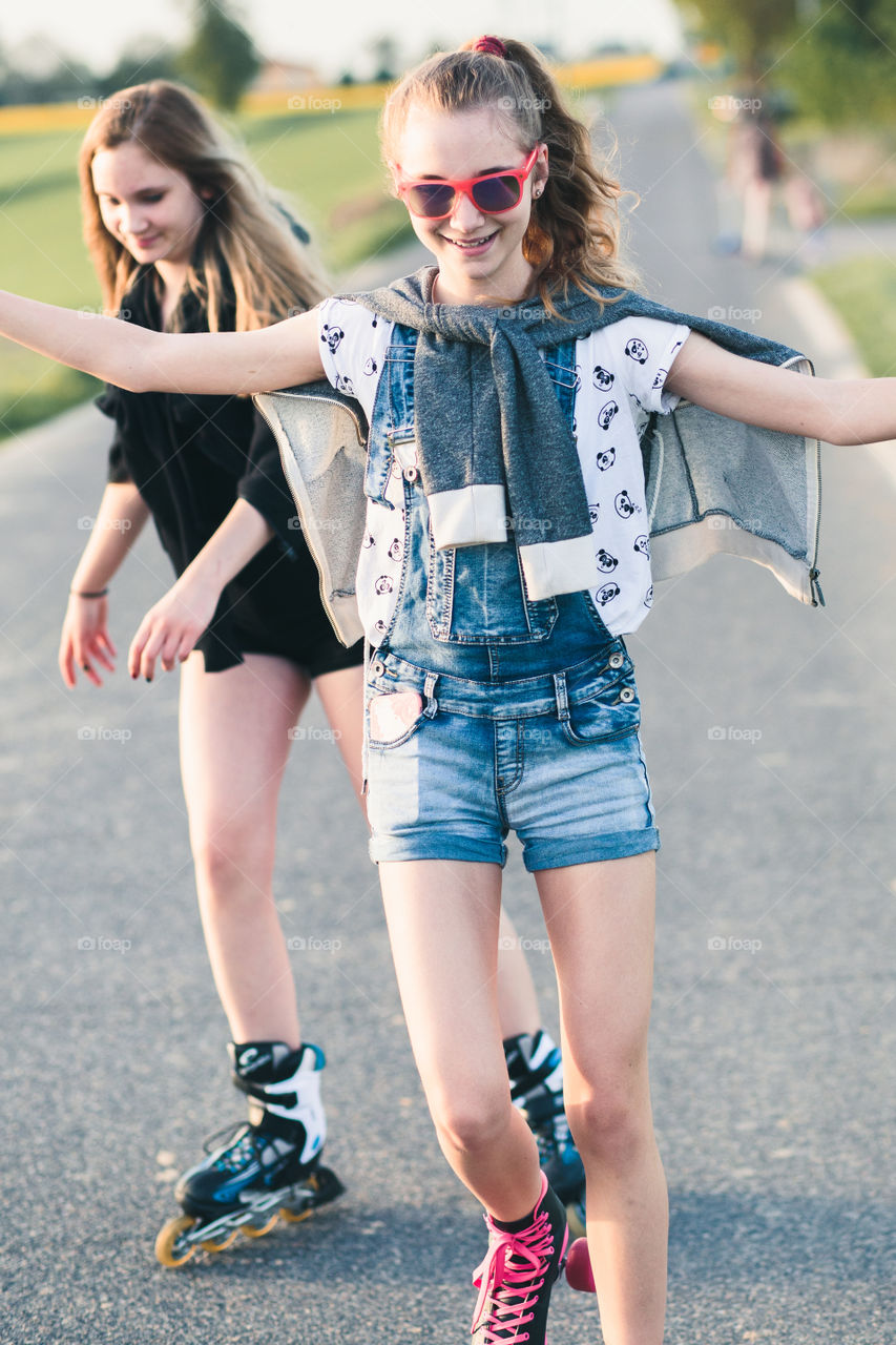 Teenage smiling happy girls having fun rollerskating together on summer day