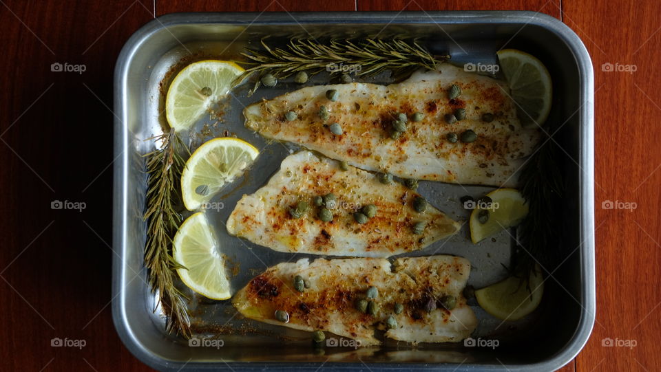 Greek cuisine - baked fish with olive oil, capers herbs and lemons