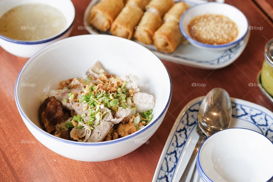 Thai street food. dried noodles with pork intestines, selective focus on the pork liver. Clear soup served on the side with spring rolls.