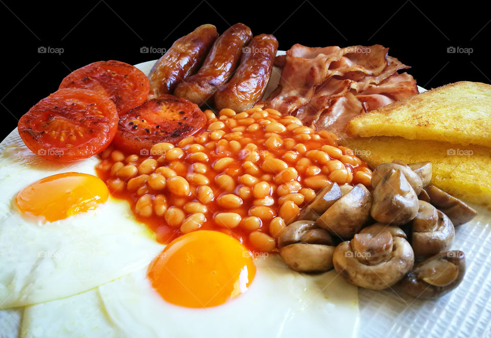 English breakfast with bacons, sausages, baked beans, eggs, mushrooms, tomatoes and toasts.