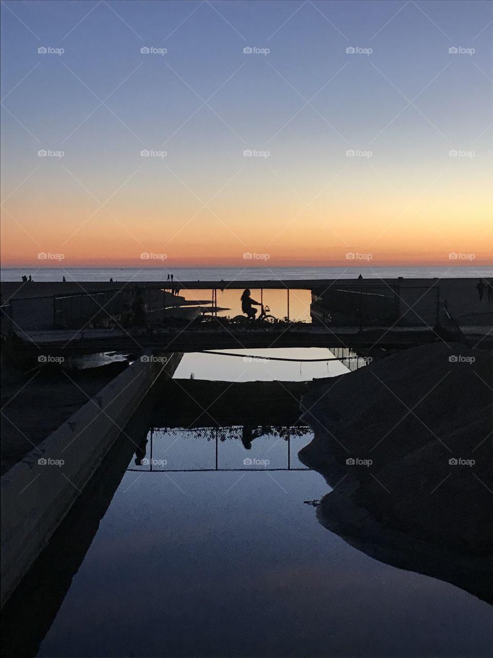 Dusk at the Santa Monica Bay with a bike rider crossing over an outlet. 